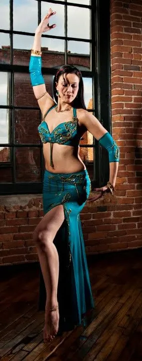 Reischa in a teal beaded costume, posing in front of a brick and window backdrop